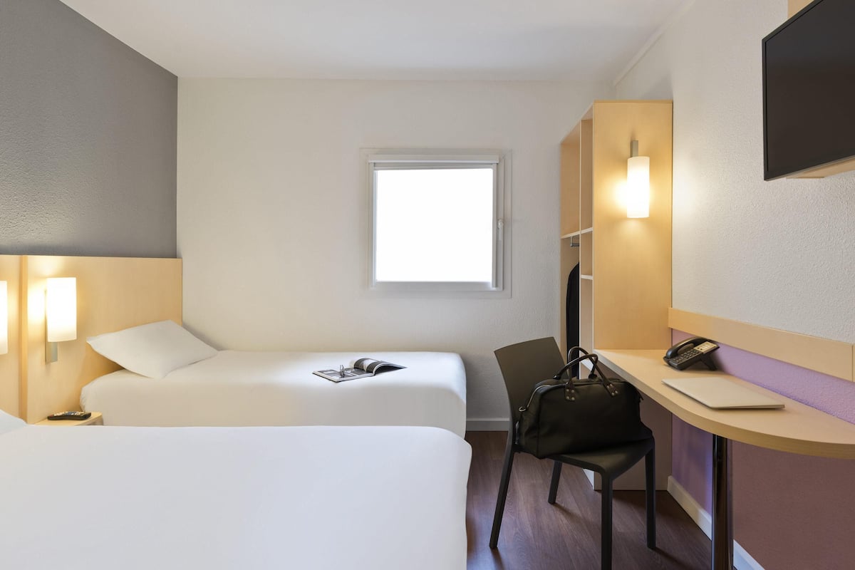 A hotel room with two beds, a desk with a chair, a telephone, and a window.