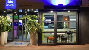 A hotel entrance with a sign for 'ibis budget hotels,' a reception area with seating, and large potted plants. - ibis budget Cannes centre ville (Cannes)