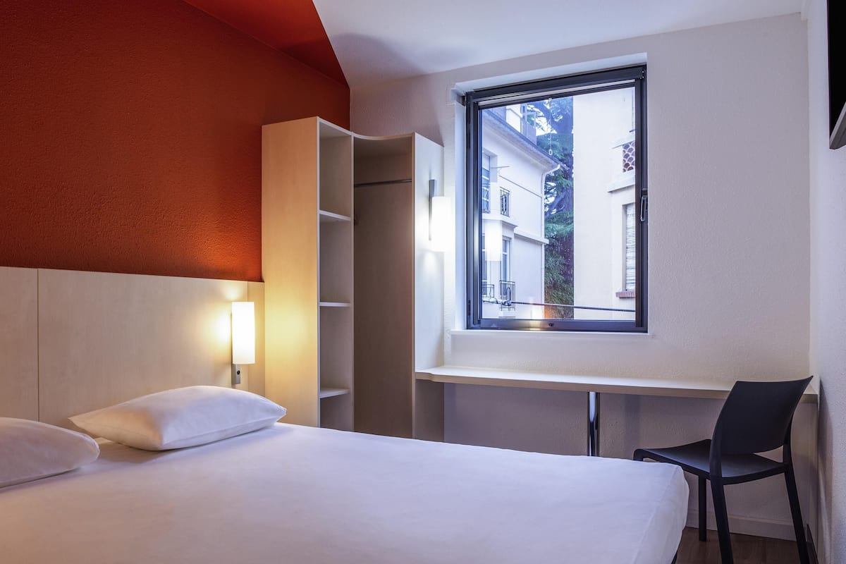 Hotelkamer met een bed, een bureau, een stoel en een raam met uitzicht op gebouwen.