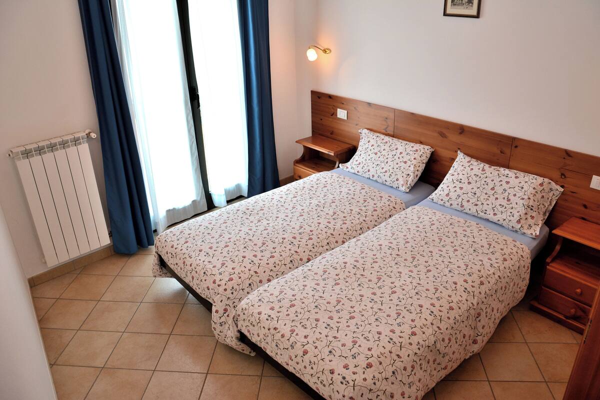 Ein Doppelbett mit floralem Bettbezug, ein Nachttisch, eine Wandlampe.