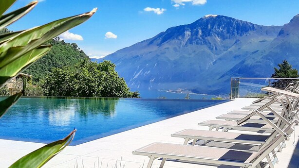 A pool area with lounge chairs, a mountain view, and a clear sky. - Stella D'Oro (Tremosine)