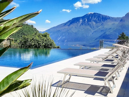 A pool area with lounge chairs, a mountain view, and a clear sky.
