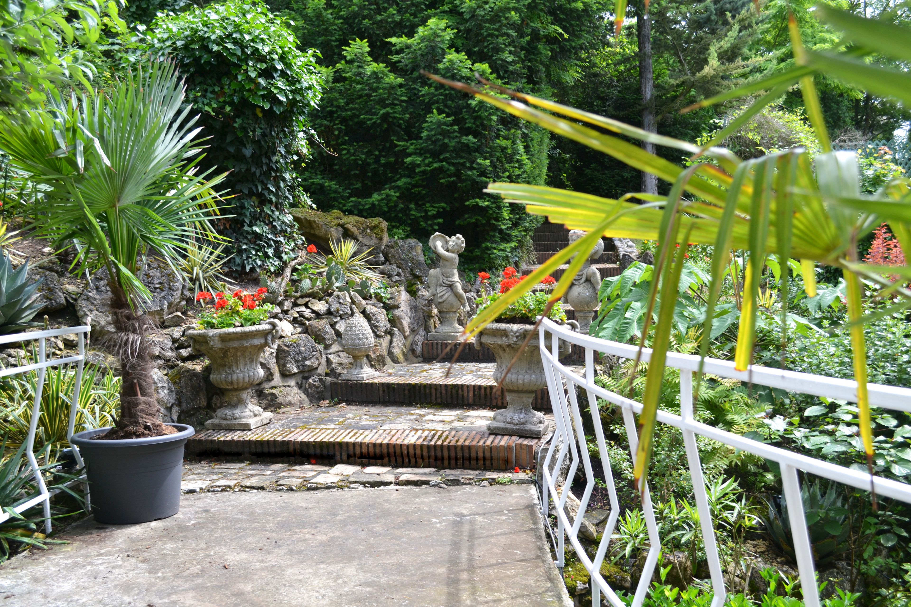 Un sentier de jardin bordé de plantes en pot et orné de sculptures en pierre.