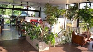 A spacious indoor area with wooden flooring, large windows, and multiple potted plants. - La Scala (Pithiviers)