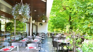 An outdoor dining area with wicker tables and chairs, surrounded by greenery and potted plants. - La Scala (Pithiviers)