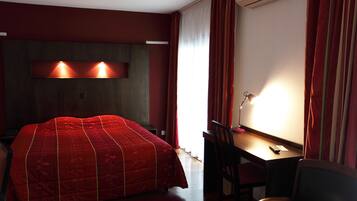 A hotel room with a large bed, a desk with a chair, and a window with curtains.