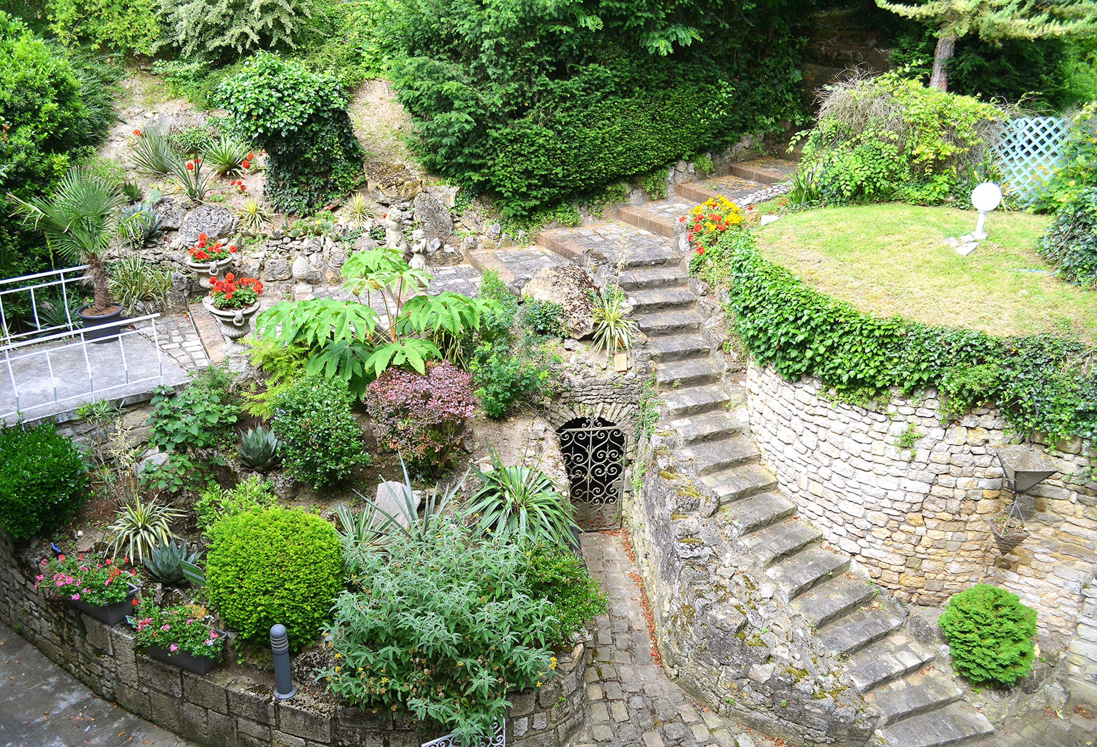 Un jardí amb escales de pedra que condueixen a una zona verda, envoltat de diferents plantes i arbustos.