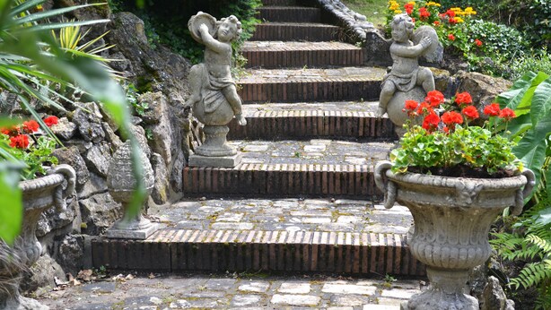 A stone staircase with statues at the top, surrounded by greenery and flowers. - La Scala (Pithiviers)
