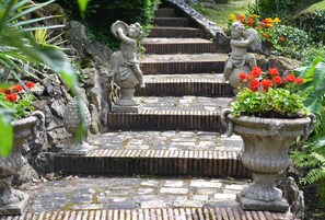 A stone staircase with statues at the top, surrounded by greenery and flowers. - La Scala (Pithiviers)