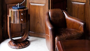A wooden interior with a leather armchair, a round wooden side table with a lamp, and two framed pictures on the wall. - La Scala (Pithiviers)