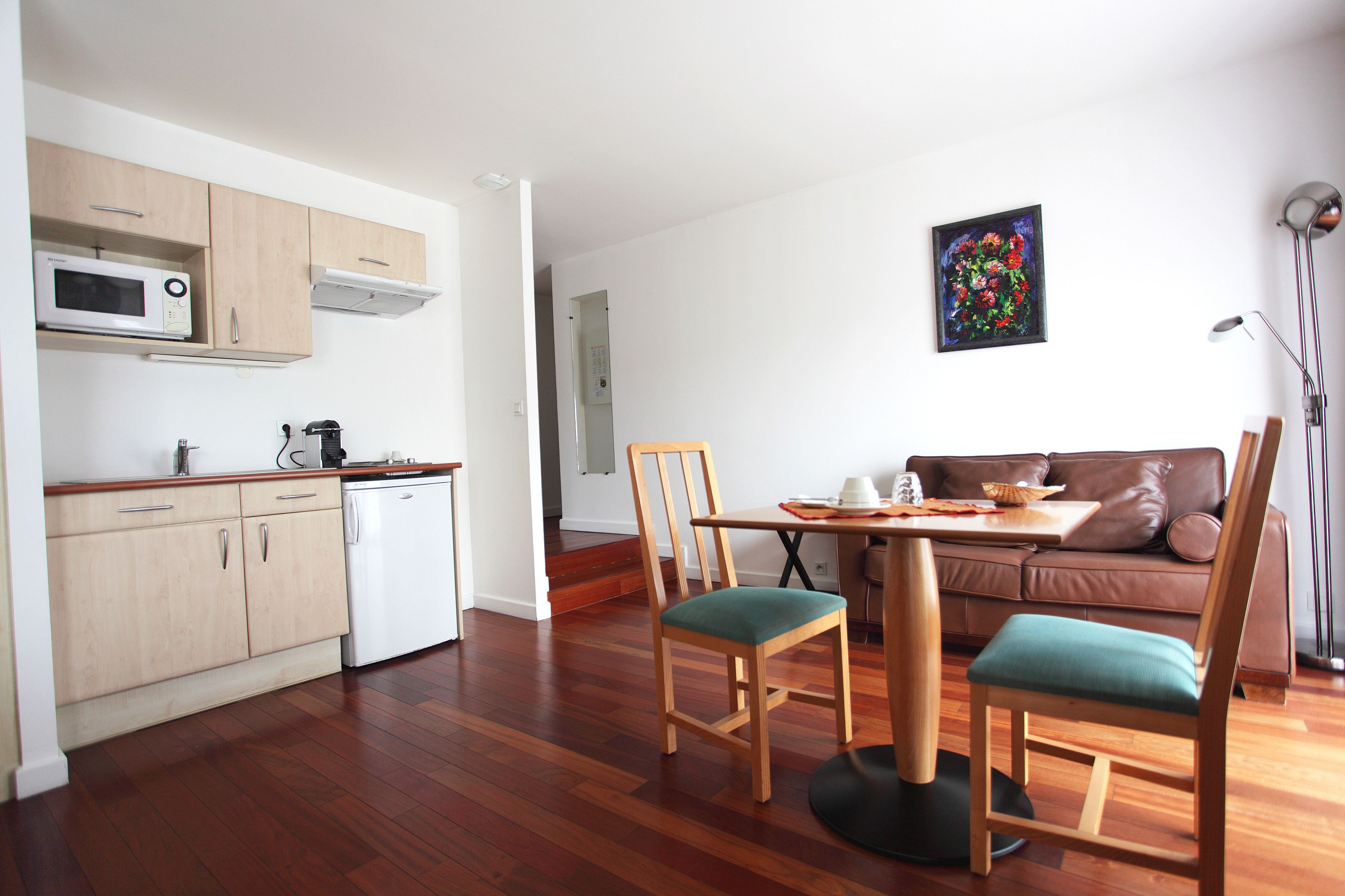 Un espacio habitable compacto con kitchenette, un área de comedor con dos sillas, un sofá y un cuadro en la pared.