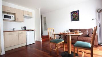 Un espacio habitable compacto con kitchenette, un área de comedor con dos sillas, un sofá y un cuadro en la pared.