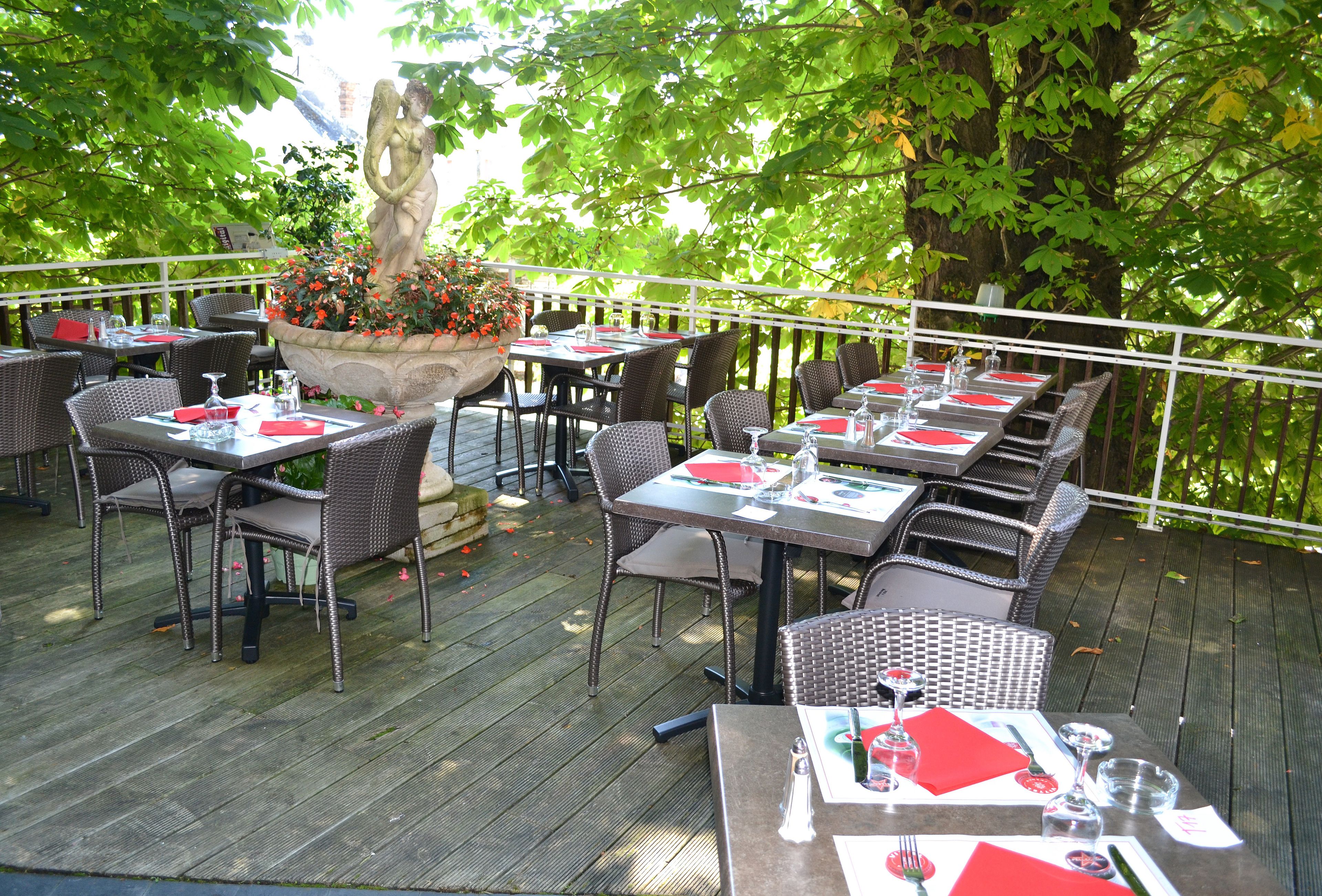 An outdoor dining area with wicker tables and chairs, a central planter with flowers, and a white railing.