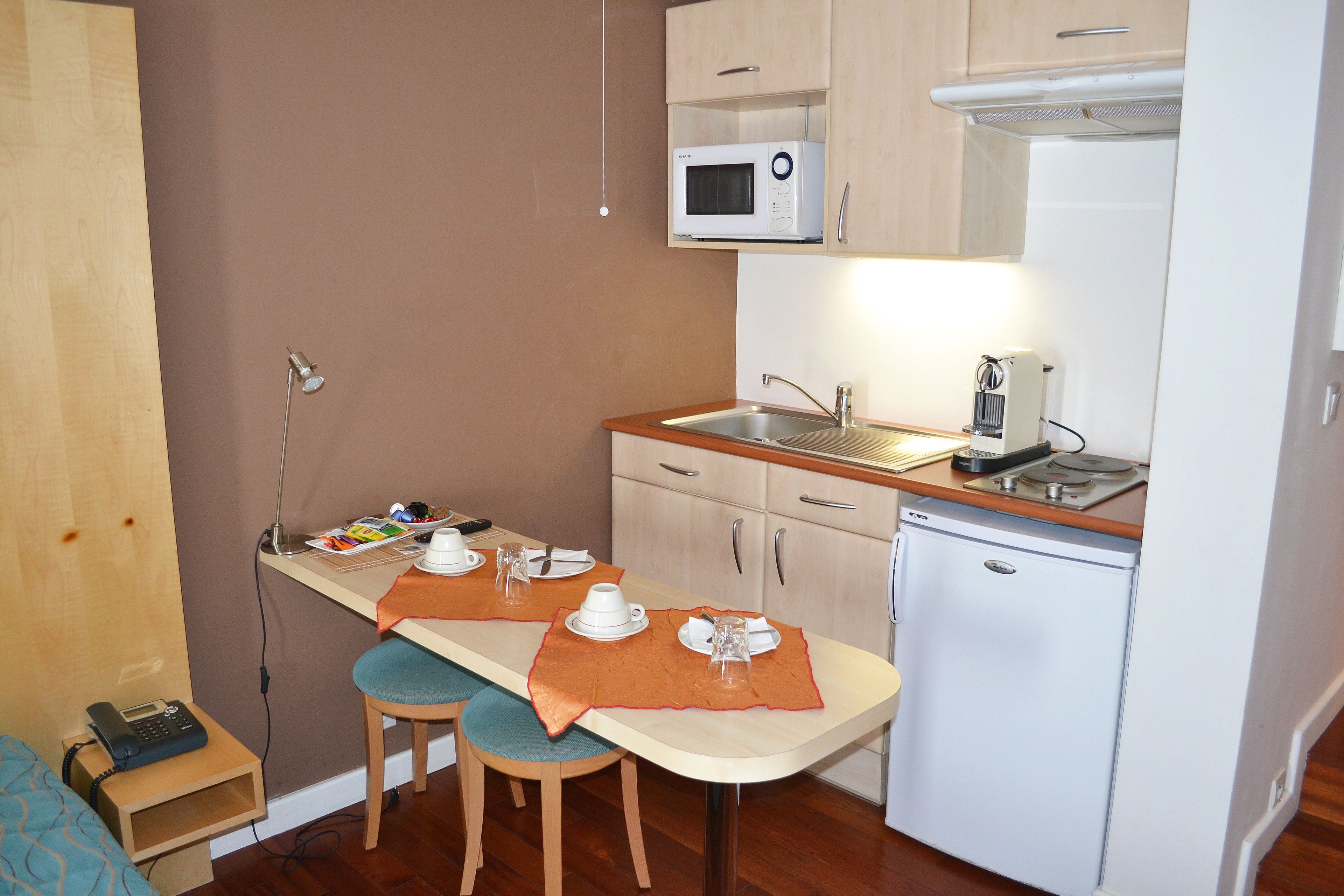 A compact kitchen with a microwave, coffee maker, and a small refrigerator. There is a dining table with two chairs and a wooden countertop.