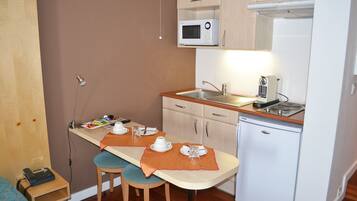 A compact kitchen with a microwave, coffee maker, and a small refrigerator. There is a dining table with two chairs and a wooden countertop.
