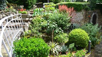 Un exuberante jardín con diversas plantas, un muro de piedra y una barandilla de metal blanco.