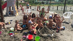 A group of children playing on a sandy beach with beach toys and a slide in the background. - Hotel Germania (Praia a Mare)