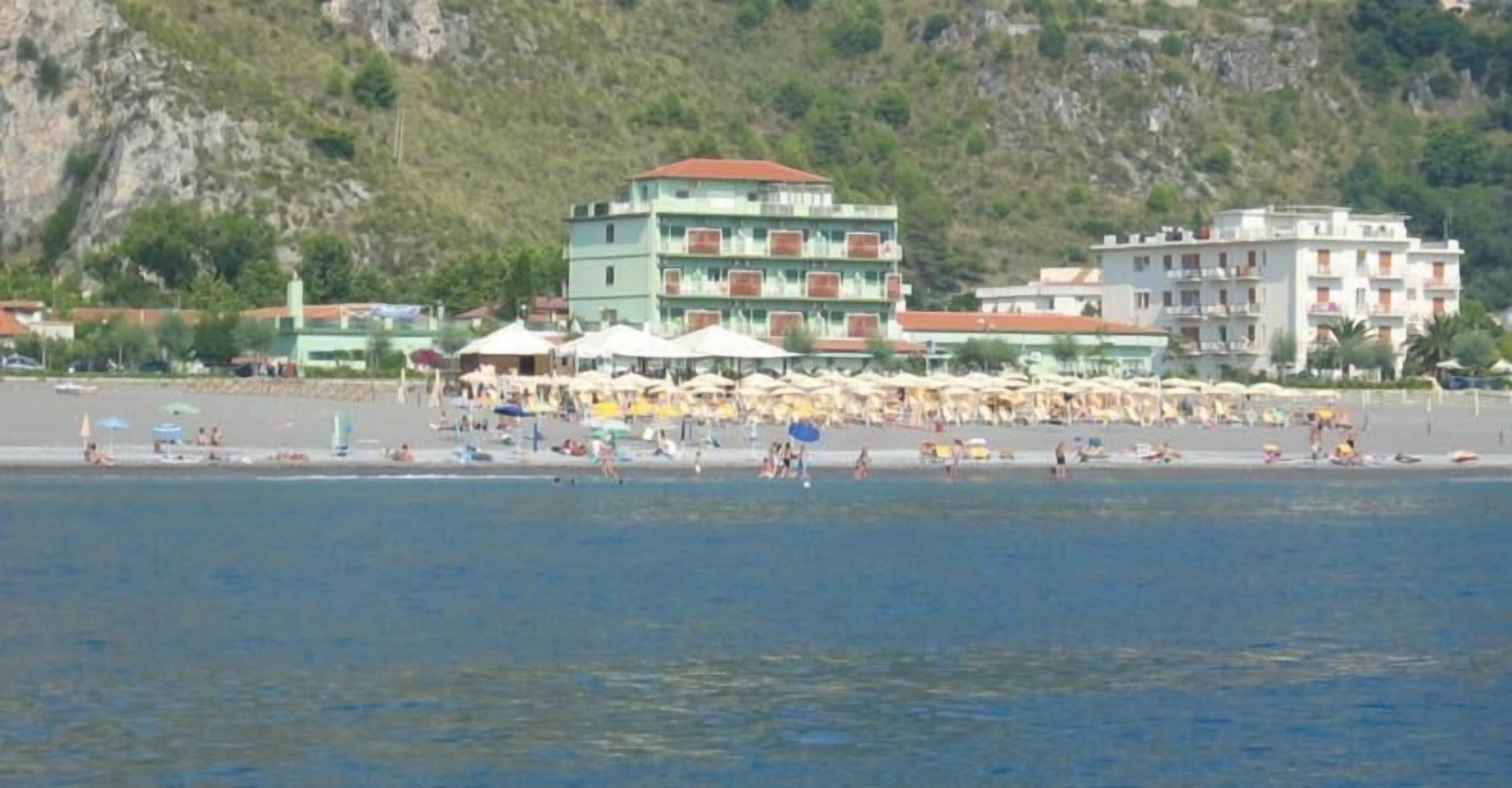 Une plage avec plusieurs bâtiments en arrière-plan, dont un immeuble à plusieurs étages doté de balcons.