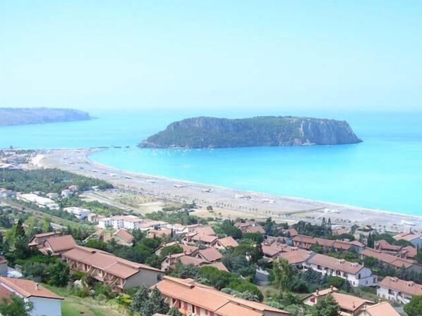A coastal town with a beach, houses with red roofs, and a cliff.