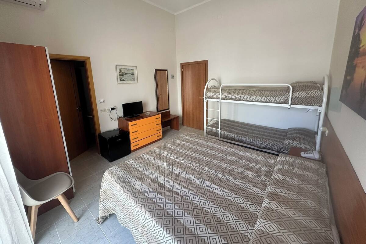 A bedroom with a bunk bed, a desk with a computer, a chair, and a wardrobe.