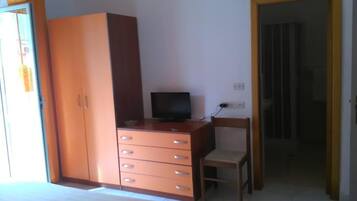 Una camera da letto con un letto, un armadio in legno, una scrivania con una sedia e una televisione.
