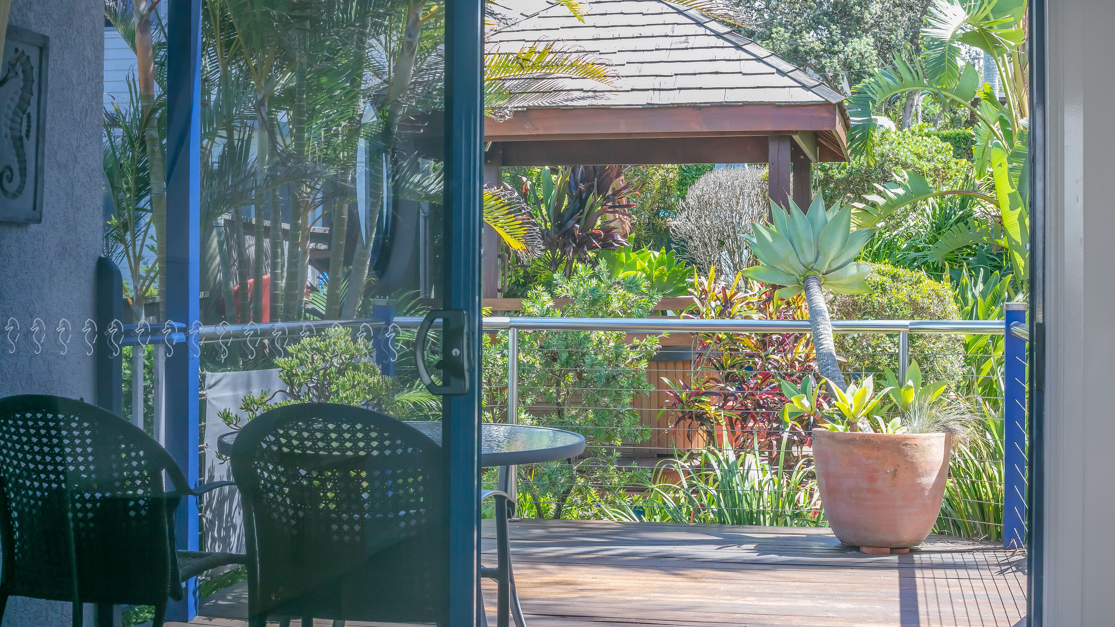En terrasse med et bord og stole, omgivet af frodig vegetation og et pergola.