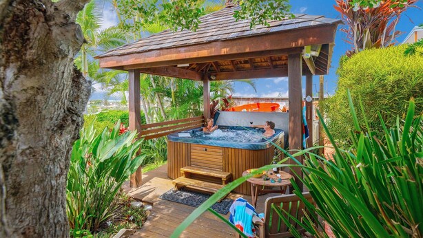 A hot tub area with wooden benches and a covered seating area, surrounded by lush greenery.