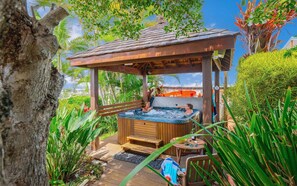 Un espace avec un bain à remous, des bancs en bois et un coin salon abrité, le tout entouré d’une végétation luxuriante.