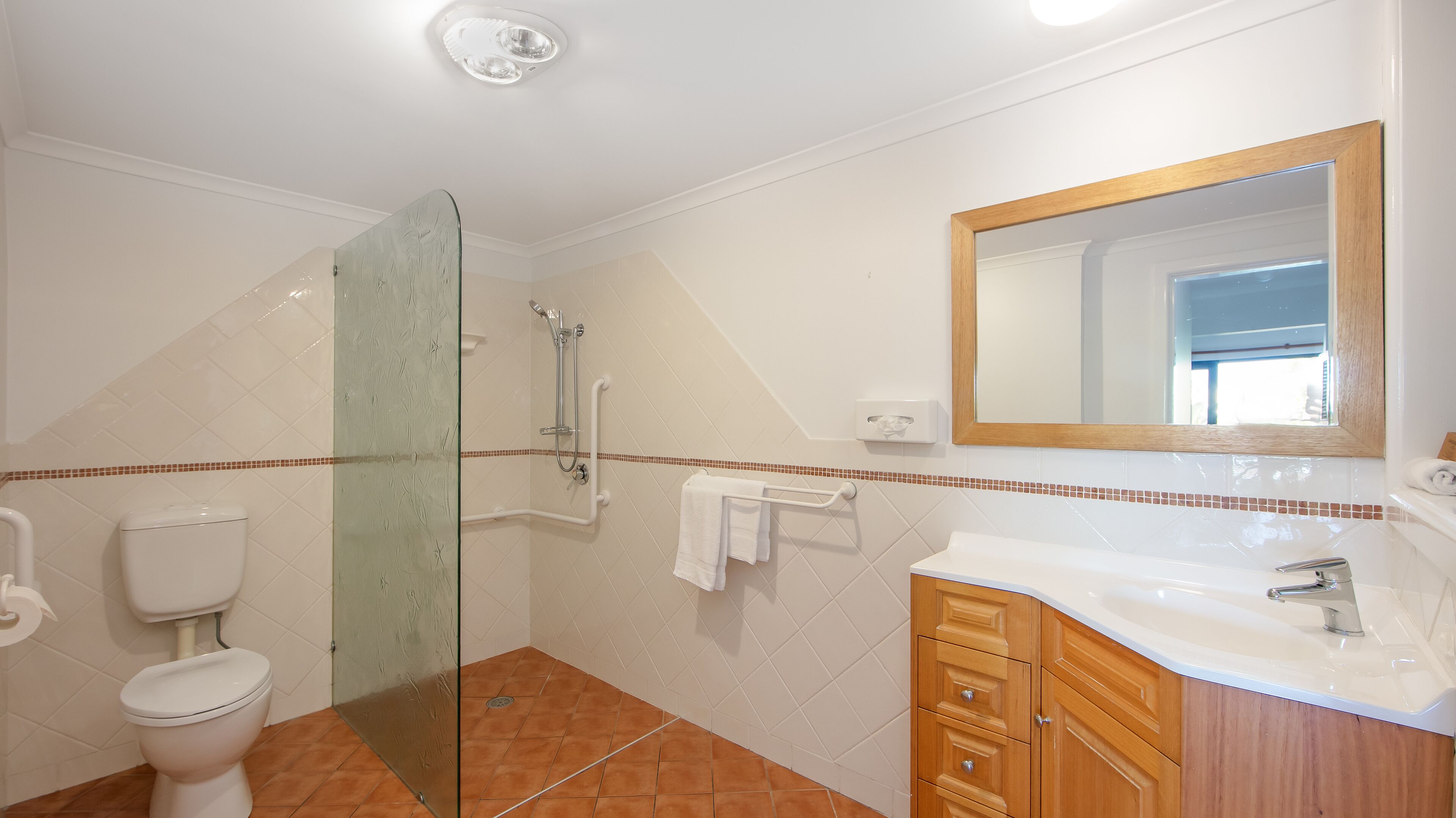 Une salle de bain avec une douche à parois de verre, des toilettes, un lavabo avec un miroir et des murs carrelés.