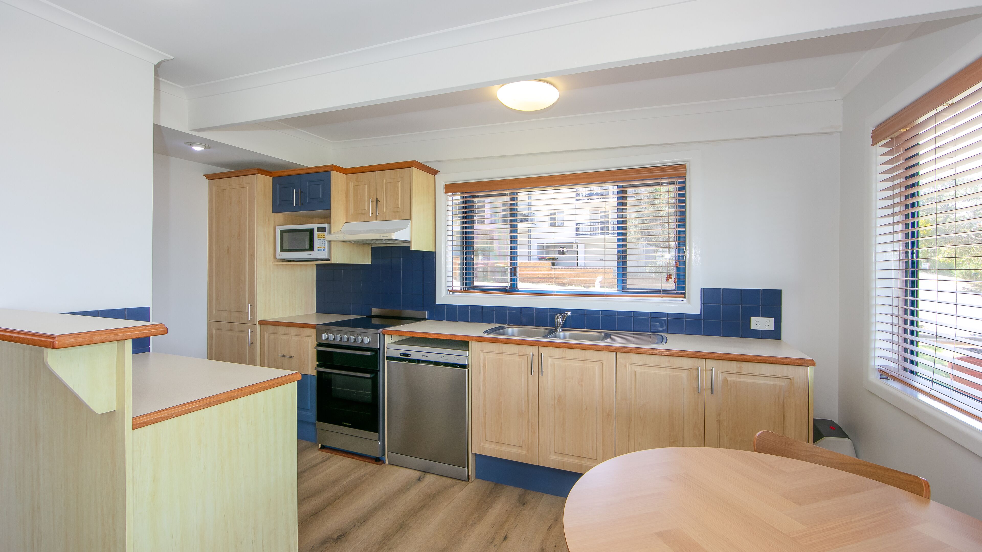 Una cocina compacta con gabinetes de madera, microondas, estufa y lavavajillas.