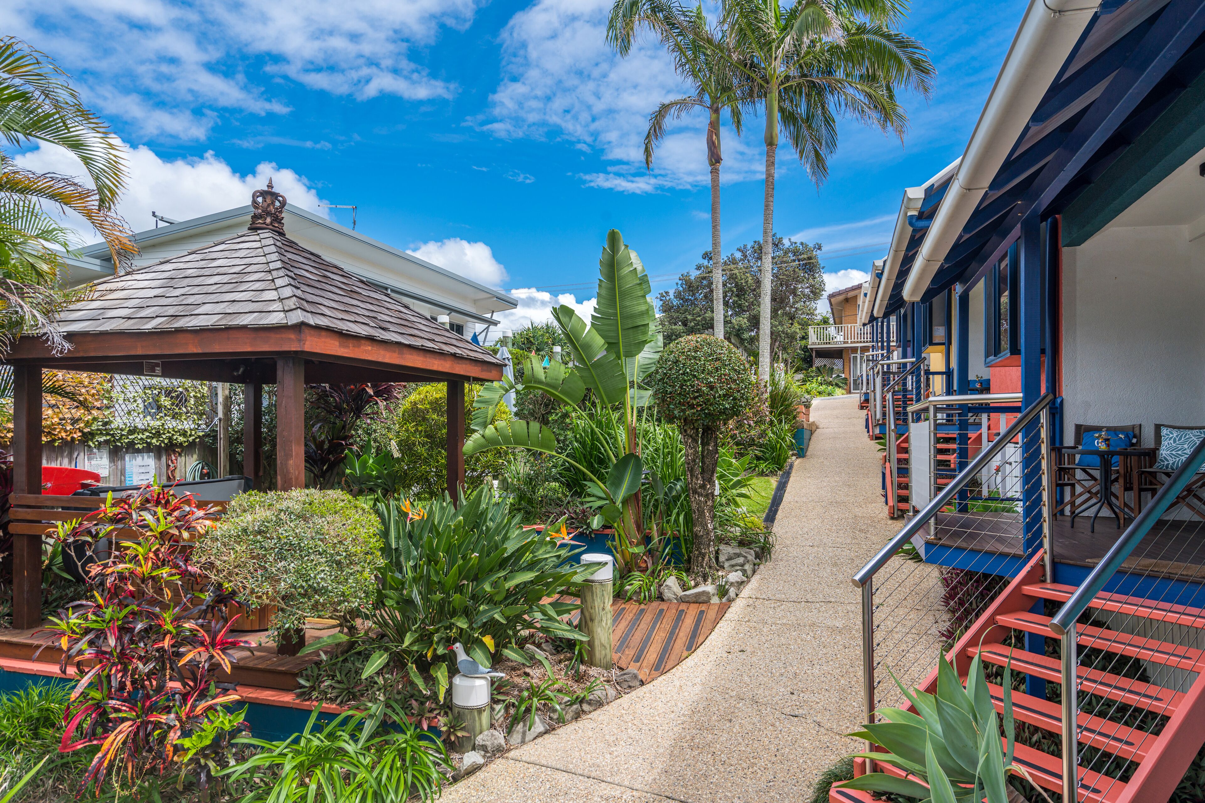 A covered outdoor area with a gazebo, a pathway, and a row of colorful buildings with outdoor seating.