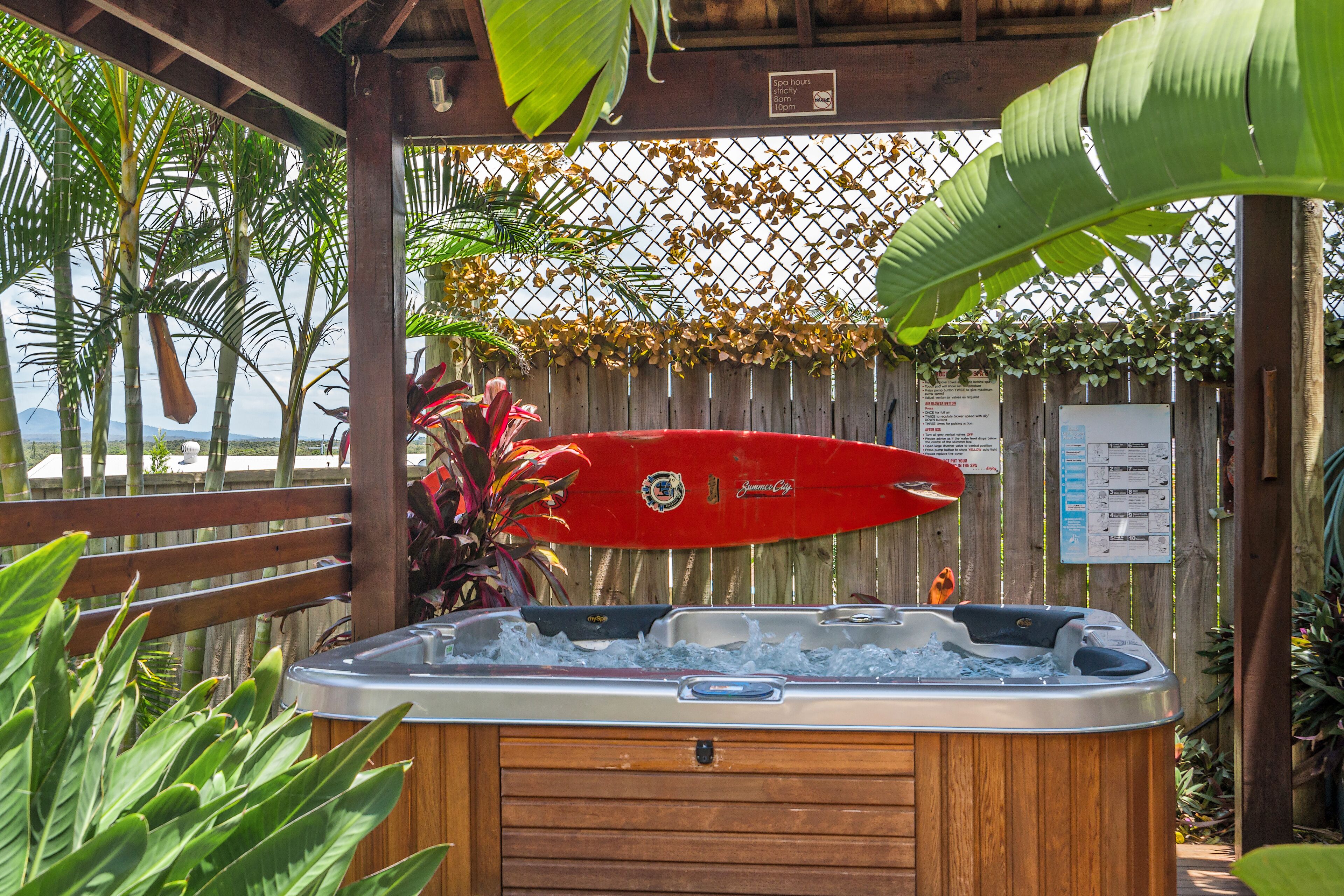 A wooden hot tub with a red surfboard and a wooden fence with plants.