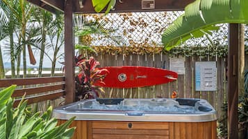 A wooden hot tub with a red surfboard and a wooden fence with plants.