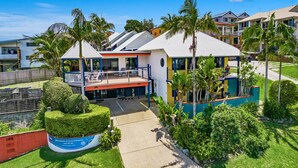 A residential building with a balcony, surrounded by lush greenery and palm trees.