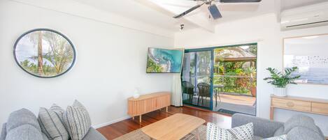 A modern living room with a ceiling fan, a large TV, a wooden coffee table, and a sofa with patterned cushions.