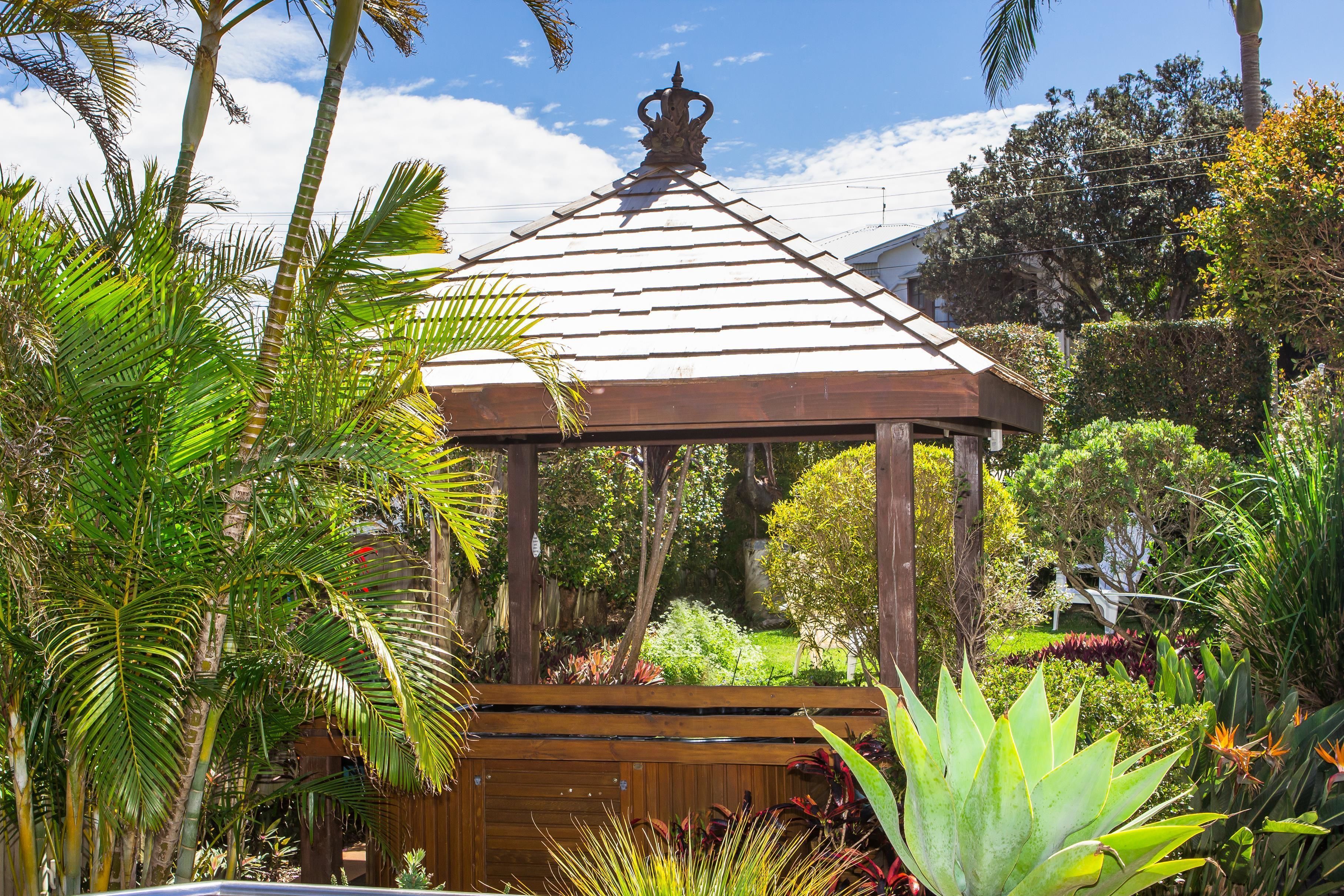 A wooden gazebo surrounded by lush tropical plants and trees.