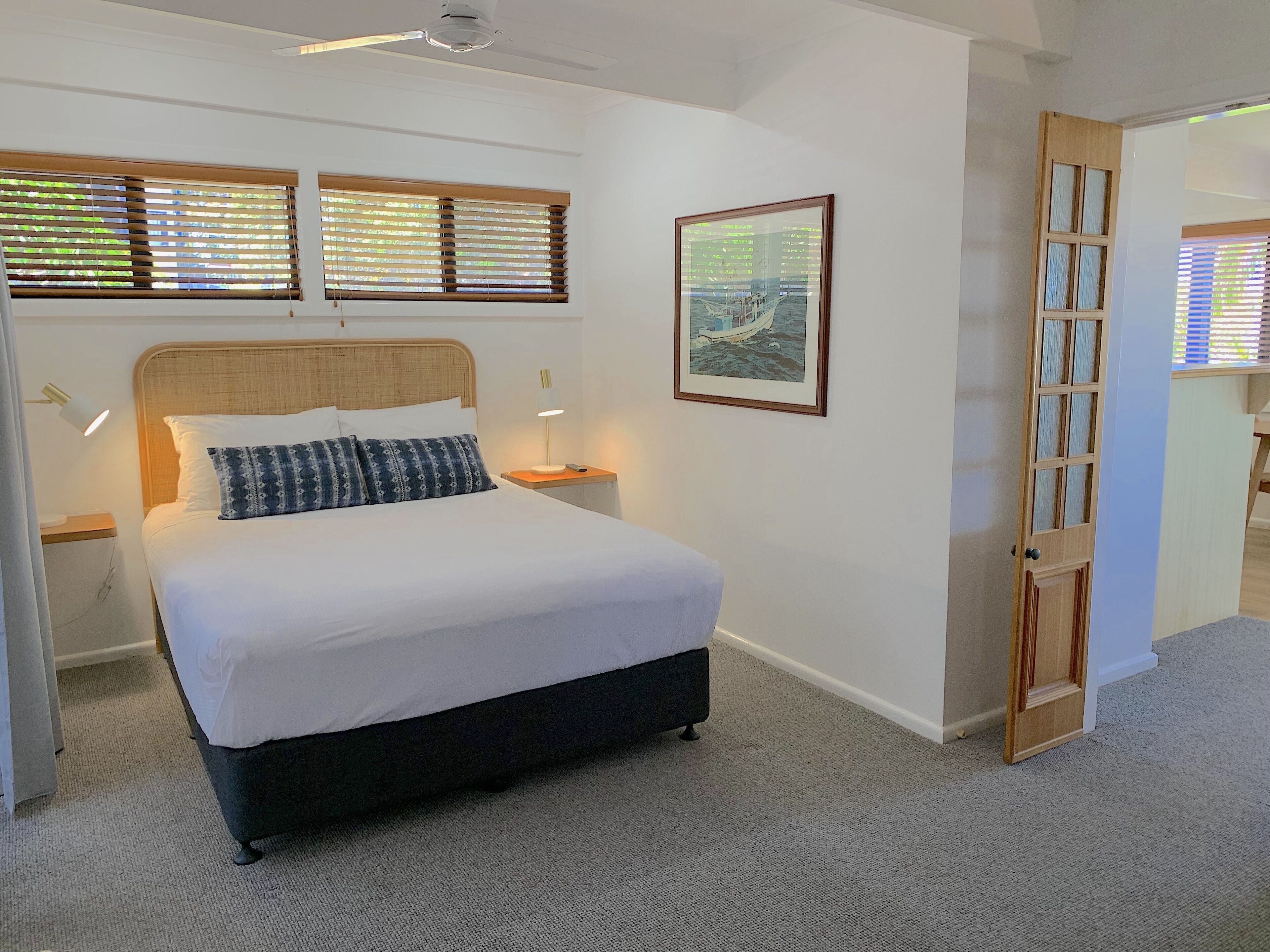 A neatly arranged bedroom with a large bed, two bedside tables with lamps, a framed picture on the wall, and a wooden door.