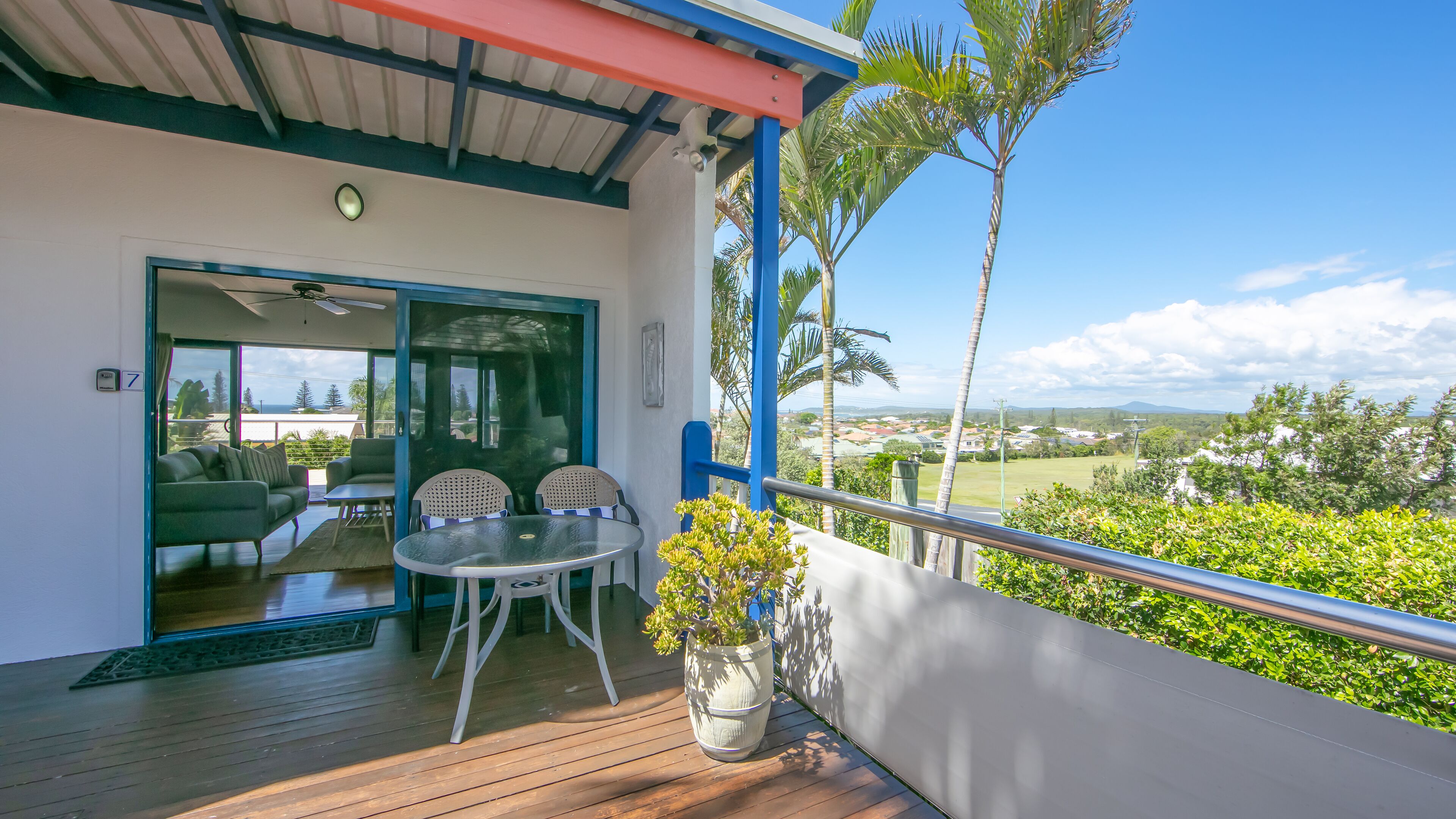 A balcony with a wooden floor, a glass door leading inside, a small table with chairs, and a potted plant.