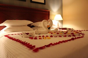 A bed with white linens, a heart-shaped arrangement of rose petals, and two swan-shaped pillows.