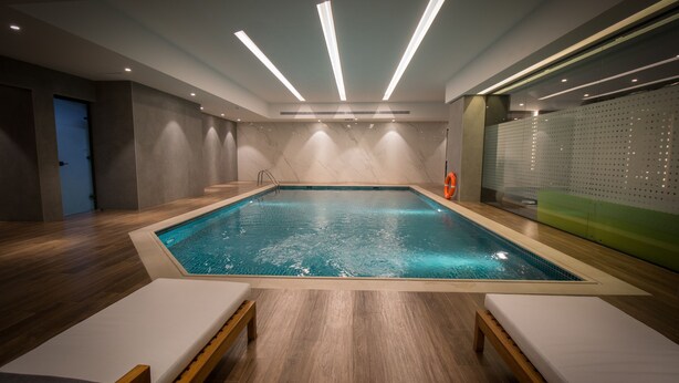 A modern indoor swimming pool with a rectangular shape, surrounded by wooden flooring and white lounge chairs. - Executives Hotel - Olaya (Riyadh)