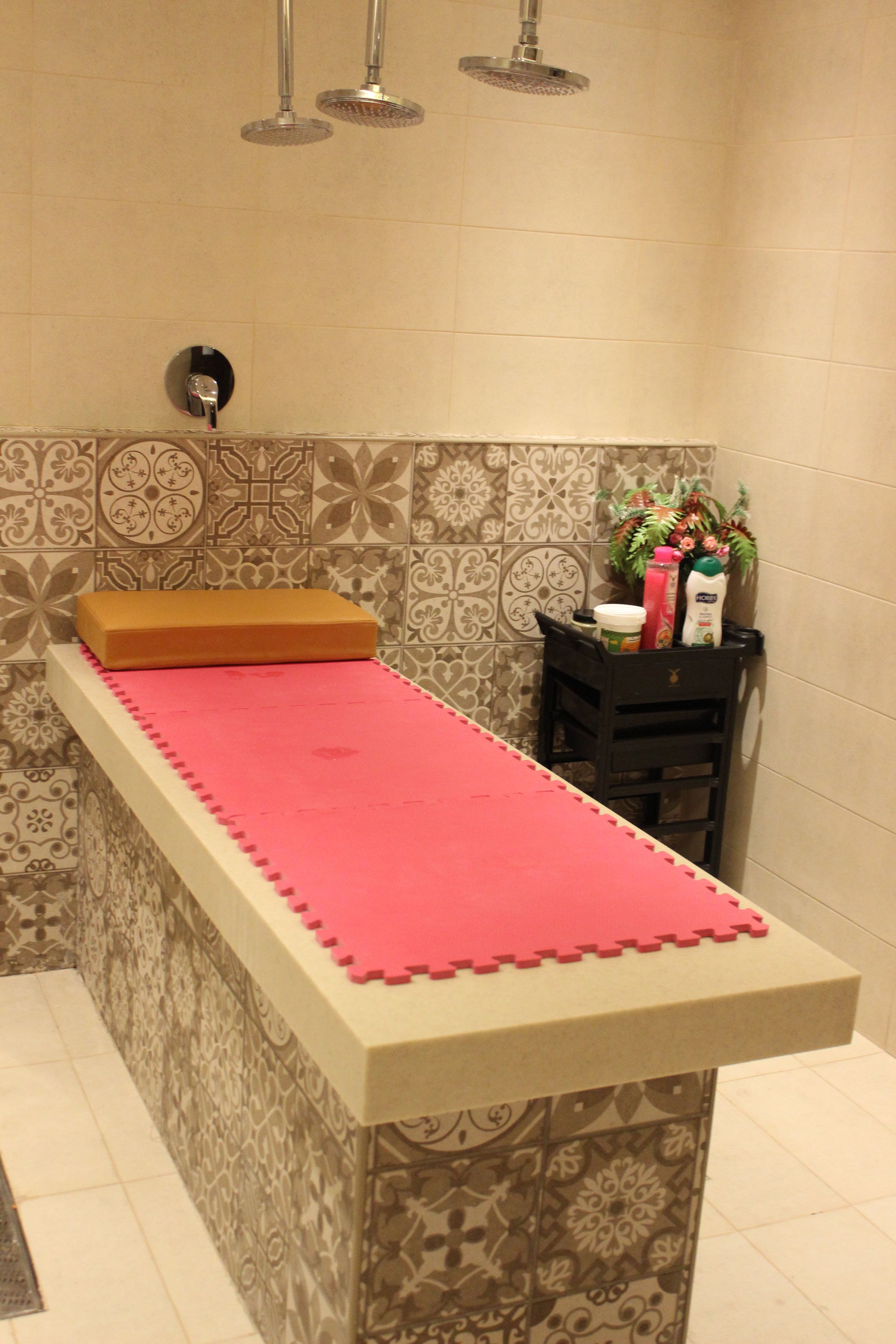 A bathroom with a shower, a sink with a pink mat, and a small table with toiletries.