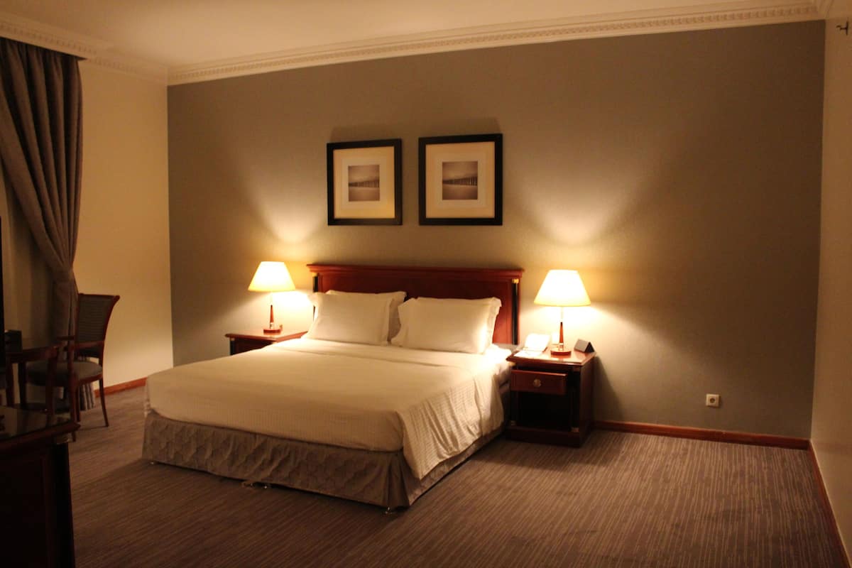 A hotel room with a large bed, two bedside tables with lamps, a chair, and two framed pictures on the wall.