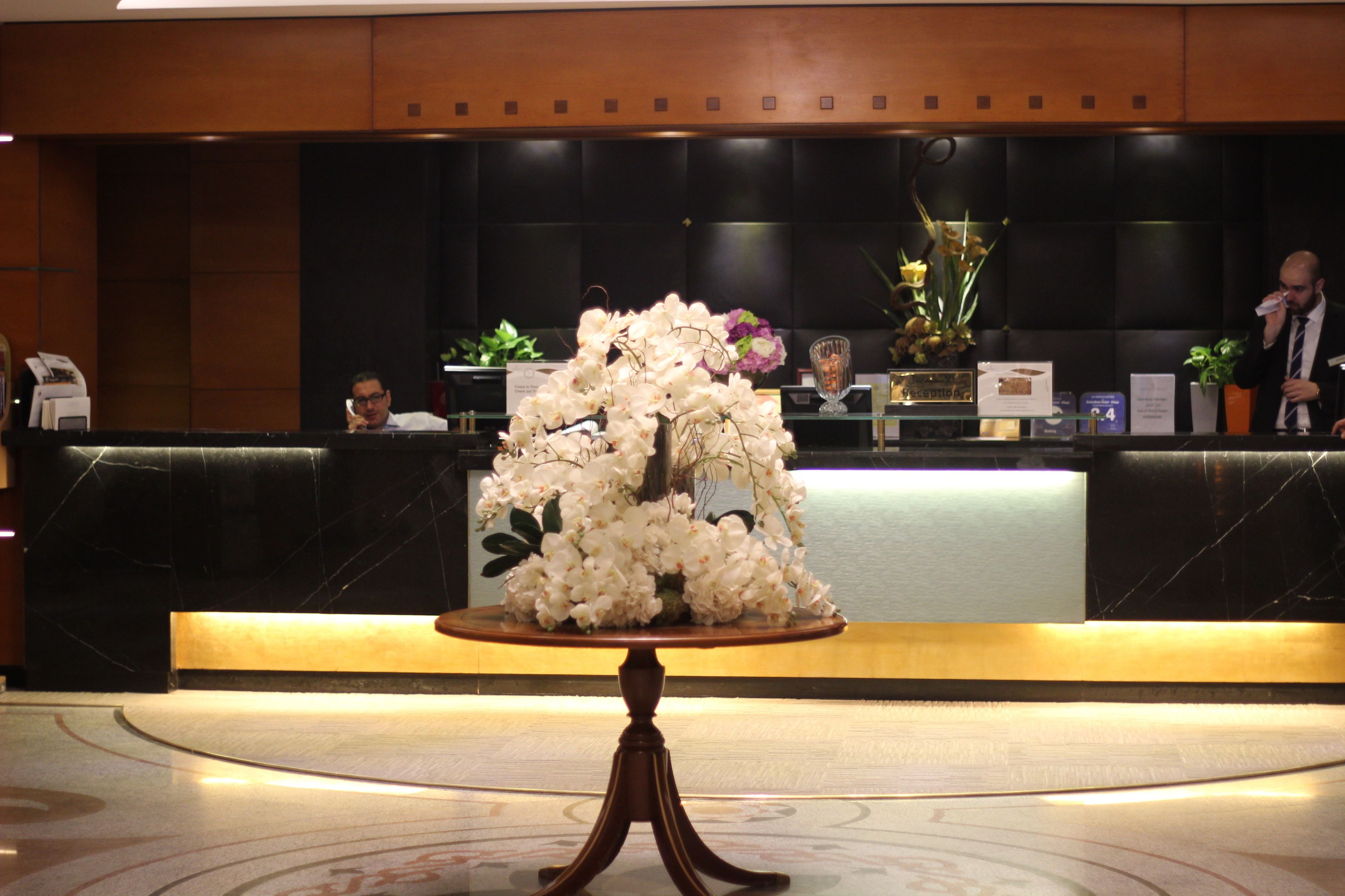A reception area with a marble floor, a reception desk, and a floral centerpiece on a wooden table.