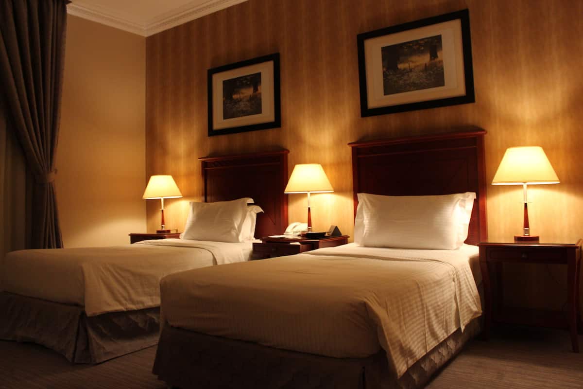 A hotel room with two beds, bedside tables with lamps, and framed pictures on the wall.