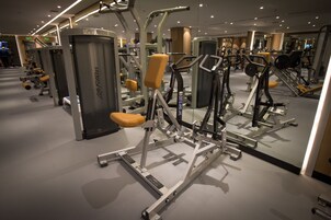 A gym with various exercise machines and a mirrored wall.