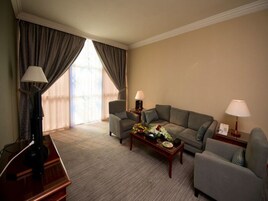 A hotel room with a sofa set, two armchairs, a coffee table, and lamps.