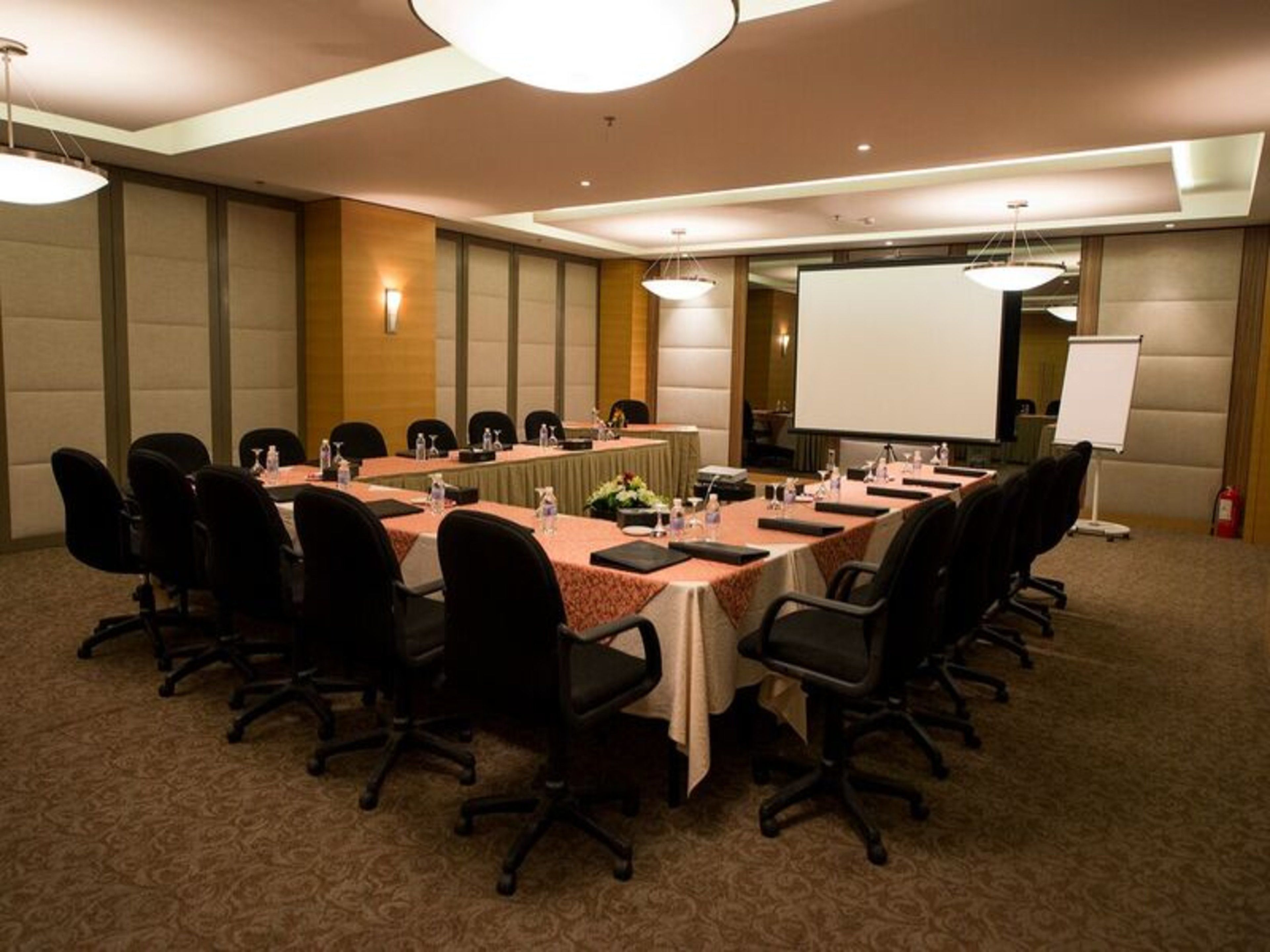 Une salle de conférence équipée d’une longue table, de chaises, d’un écran de projection et d’un tableau blanc.