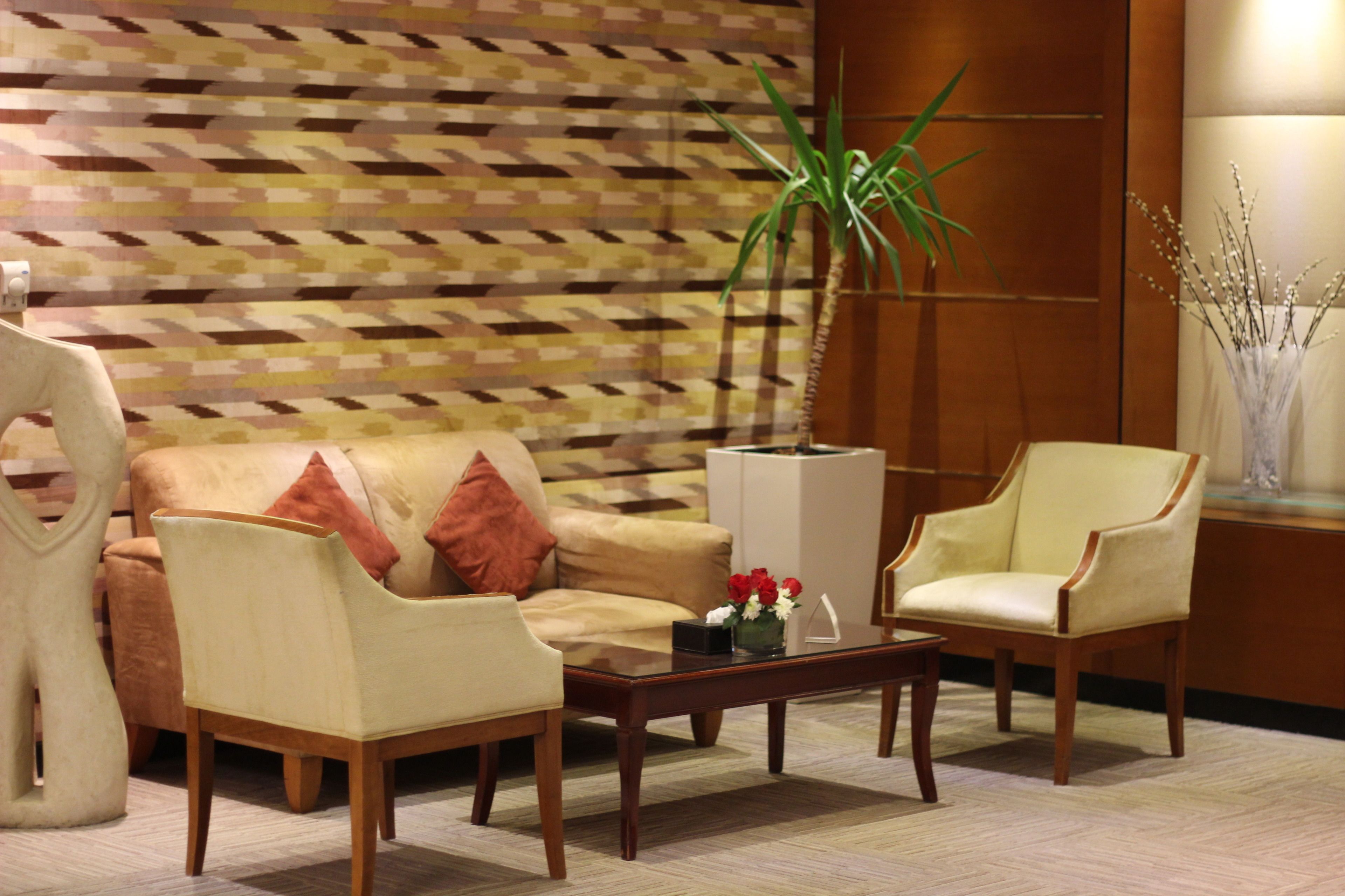 A modern living room with a patterned wall, a sofa, two armchairs, a coffee table, and a potted plant.