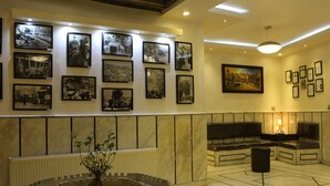 A lobby with a marble reception desk, a seating area with a fireplace, and a wall adorned with framed photographs. - Arab Tower Hotel (Amman)