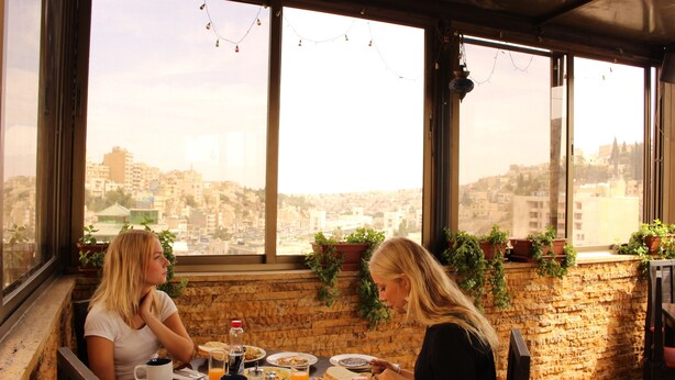 Two people dining at a table with a city view, a brick wall, and potted plants. - Arab Tower Hotel (Amman)